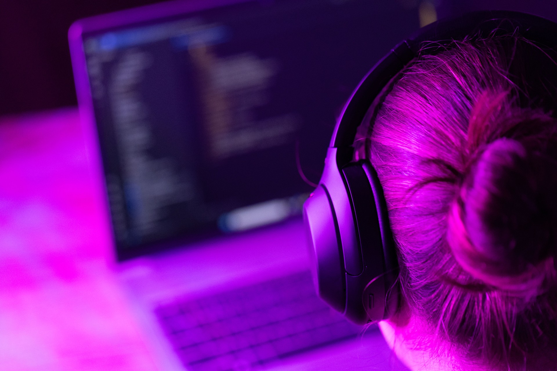 woman software developer in modern wireless headphones against laptop screen with software code