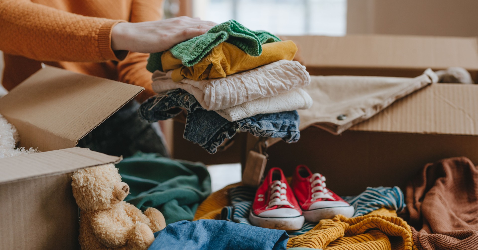 Woman sorting an old out-of-use kid toy, clothes and shoes in box for charity or upcycling